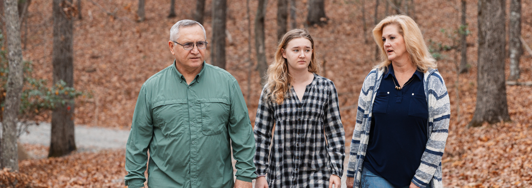 Adoptive parents and child walking in the woods in autumn.